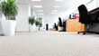 © Nusaba - Modern Office Space: An empty, well-lit, modern office interior with a focus on a clean, light-colored carpet, highlighting the arrangement of office furniture, desks, chairs, and potted plants.