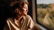 © GATE 22 - Young woman sitting on a train, looking out the window with her eyes closed and a peaceful expression on her face. she is wearing a beige blouse and her hair is styled in loose curls.
