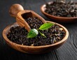 © enggis - Dried black tea leaves in wooden bowl with fresh green tea leaf on dark table background, organic herbal tea concept