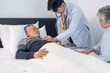 © Verin - asian male doctor using stethoscope to examine elderly patient lying in bed while his senior wife supporting beside