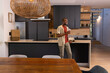 © wavebreak3 - African American man standing at marble kitchen island leaning, holding drinking glass, smiling