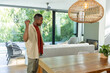 © wavebreak3 - African American man standing at home by wood dining table raising fist, looking toward glass doors