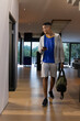 © wavebreak3 - African American man mid-20s walking through home wearing hoodie carrying duffel bag holding phone