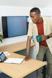© wavebreak3 - African American man leaning at light wood desk, reviewing tablet and charts, holding green mug