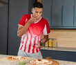 © wavebreak3 - Adult man tasting seasoning while preparing two pizzas in kitchen wearing striped shirt with basil