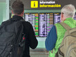© luciano - Two Travelers Checking The Airport Departure Board At Information Desk In Terminal