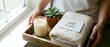 © Yuliia - Hands holding a wooden tray with a lit candle, folded towel, succulent plant, and self care card for wellness and spa concepts.