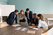 © fizkes - Group of diverse team members gathered around conference table, discussing online project displayed on laptop, engaging in corporate briefing, strategy planning, business application review in office