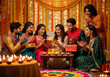 © Nokkz - Happy Indian friends and family celebrating Diwali, smiling while opening gifts in a beautifully decorated home with diyas and warm festive lighting.