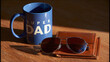 © Алексей Иванченко - Blue super dad mug with sunglasses and a leather wallet on a wooden table in soft morning light for Father's Day concept celebrating paternity and love