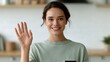 © Chandlerlikes - Young woman holding smartphone and waving during video call in bright kitchen, cheerful remote communication concept