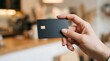 © Syauqiya - Close-up of a hand holding a sleek black credit card with a gold chip.