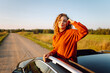 © maxbelchenko - A traveler leans out of a car window at sunset. A young woman enjoys the rural landscape during a road trip. Concept of freedom and enjoyment and transport.