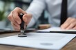 © Daniel - Corporate employee applying stamp to official document in office setting, illustrating business approval process, administrative workflow, and professional paperwork management.