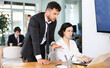© JackF - Male employee of the bank office stands near table and helps woman to fill out documents and bills on a laptop. Office employees are working on a project and checking data on a laptop