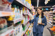 © anatoliycherkas - Woman choosing liquid detergent in supermarket, comparing products and shopping for household supplies