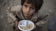 © A2Z AI  - Young child in worn clothing looks up with a pleading expression, holding a simple plate with a small portion of rice, against a muted background