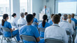 © FrameFlow - Healthcare professionals lecture audience, medical doctor speaking from podium next to projector screen, sitting in rows of chairs, bright hospital seminar hall, professional photography