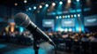 © Masque - Close-up of a professional microphone on a stand during a live event with a blurred audience.