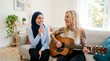 © insan - Hijab Woman Singing With Tattooed Blonde Friend Playing Guitar In Minimalist Living Room