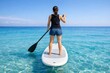 © Jumpei - 透明度の高い青い海でスタンドアップパドルボードを楽しむ後ろ姿の女性と美しい夏の景色