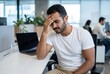 © Asier - Young man experiencing pain and burnout while working on his laptop in the office