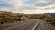© dewi - Scenic Route 66 Highway Winding Through Arid Desert Landscape at Sunset.