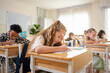 © JU.STOCKER - Diverse group of elementary students studying in classroom, Concentrated students writing at their desks in modern school, Children learning together in a bright primary school classroom