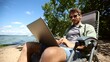 © ASDF - A man is sitting on a beach chair with a laptop in front of him