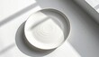 © Nayy - A white plate sits on a surface with shadows from a window.