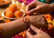 © Uttara Graphic - A sisters caring hands tie a beautiful rakhi bracelet onto her brothers wrist during a cherished festive celebration with sweets and lights
