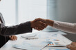 © Crystal - Two business colleagues shaking hands over a desk with documents, agreeing on a new business partnership and collaboration