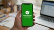 © Alex Pios - Person holding smartphone displaying payment successful screen with work desk in the background.