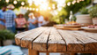 © Nataliya - Rustic wooden table overlooking a lively outdoor barbecue scene bathed in warm sunlight, summer entertaining concept, defocused background, with copy space