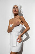 © sutulastock - Woman wrapped in white towel with hair towel standing against white wall, enjoying spa wellness moment with closed eyes, natural light, minimal self care concept and relaxation