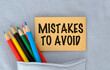 © Pawel - Colorful pencils lean near a sticky note. Note reads MISTAKES TO AVOID in bold black letters. Note rests in a folded fabric pocket.