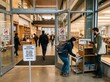 © Sendy - No food or drink sign at a library entrance with a visitor putting away beverages, realistic public facility regulation and cleanliness concept.