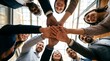 © haemye - Group of diverse professionals gather in a high-ceilinged office space. They form a unified hand stack, smiling broadly at the camera. Their joyful expressions convey teamwork and shared success