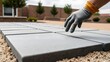 © ModernFiles - Hands lowering a heavy gray concrete slab onto a sand base in a private courtyard, dramatic side light.
