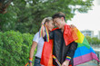 © ฺฺฺBoonterm - Gay couple LGBTQ community strolled through nature park waving brightly colored Prime Minister's flag openly displaying affection through intimate hugs kisses demonstrating proud connection community.