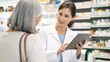 © Christos - Pharmacist consulting senior woman using digital tablet in modern pharmacy interior