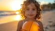 © EBG Stock Studio - Niña pequeña sosteniendo una pelota naranja en la playa al atardecer con luz cálida de verano