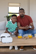 © wavebreak3 - Sitting African American father and boy gaming on couch holding white controllers VR headset nearby