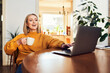 © baranq - Woman using laptop and drinking coffee at home dining table