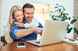 © baranq - Couple laughing together while using laptop at home