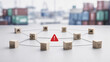 © vatcharapong - supply chain management logistics risk management. Wooden blocks with supply chain icons connected by lines and a red warning triangle in the center, blurred containers back...