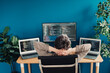 © deagreez - Relaxed software developer leaning back at a home office desk with three monitors coding on laptops and a large screen — productive remote work and focused programming setup