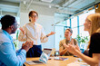 © we.bond.creations - Business executive presenting to colleagues in a modern office meeting, team members are clapping, showing appreciation and success