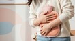 © Pete - Woman holds pink hot water bottle to stomach. She feels period pain. Uses heat for cramp relief. Gentle therapy for monthly discomfort. Feels better with warmth. Comforting relief at home. Feels calm.