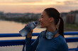© Home-stock - Young caucasian female athlete drinking water during outdoor fitness training at sunset